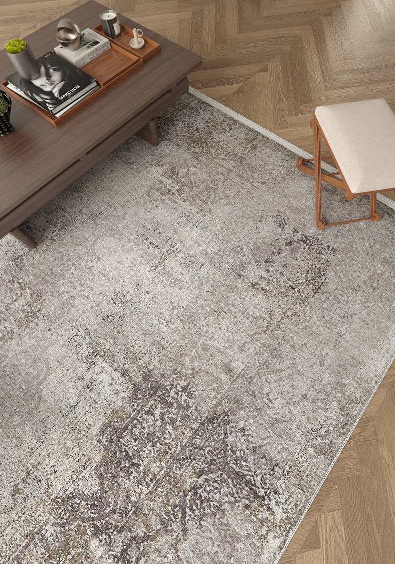 A modern living room with the Noble Insignia – Washable Rug – JR1830 (Outlet) US in light gray pattern on herringbone wood floors, paired with a low wooden coffee table and a small stool—ideal for high-traffic spaces.