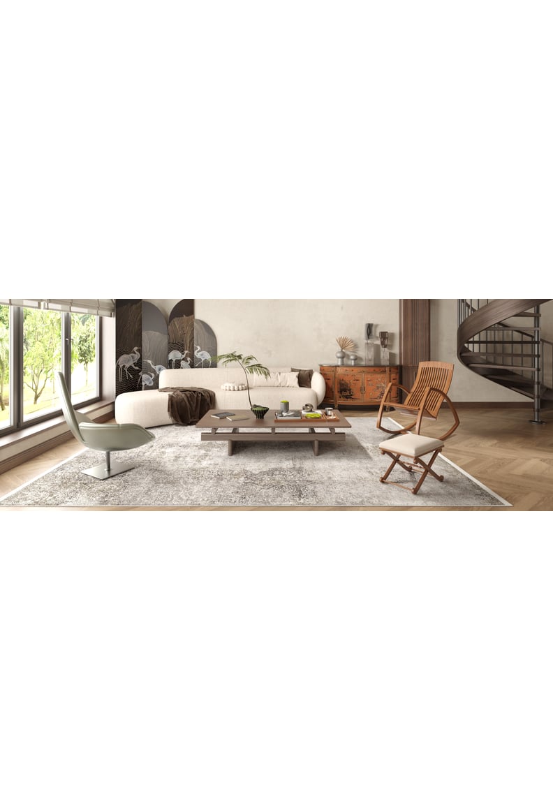 A modern living room with large windows, a white sectional, wooden coffee table, tan chairs, and the Noble Insignia - Washable Rug - JR1830—perfect for high-traffic spaces. Decor features plants, wall art, and a spiral staircase in the background.