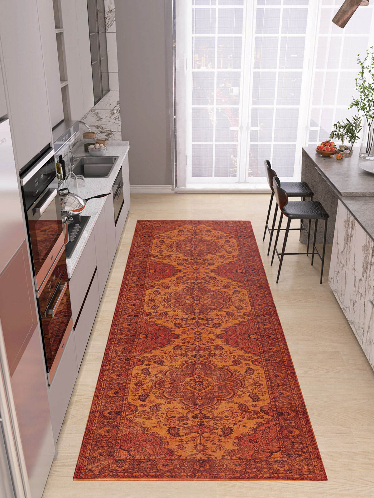 A modern kitchen with light wood floors, white cabinets, and gray countertops features the Noble Odyssey - Washable Rug - JRN1012 with a red and orange medallion design, centered between bar stools and large windows draped in sheer curtains.