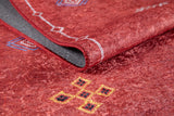 A close-up of the Nomadic Journey - Washable Rug - JR5080 (Custom Size) shows red geometric patterns in yellow, blue, and white. The partially folded rug reveals a grey underside and stitched edge—ideal for high-traffic spaces.