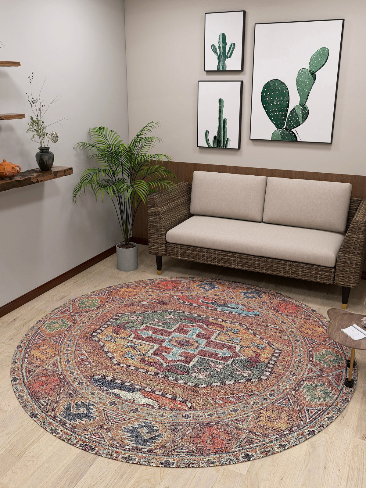 A cozy room with a beige sofa, potted plant, and cactus wall art. The Nomadic Oasis - Washable Rug - JR5086 (Custom Size) is ideal for high-traffic, allergy-sensitive spaces, paired with a side table and wooden shelf on light wood floors.