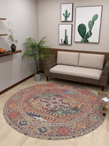 A cozy room with a beige sofa, potted plant, and cactus wall art. The Nomadic Oasis - Washable Rug - JR5086 (Custom Size) is ideal for high-traffic, allergy-sensitive spaces, paired with a side table and wooden shelf on light wood floors.