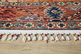 Close-up of the edge of the Nomadic Oasis - Washable Rug - JR5086 (Custom Size), featuring colorful geometric patterns, white fringe tassels with red and blue thread, ideal for high-traffic areas, shown on a wooden floor.