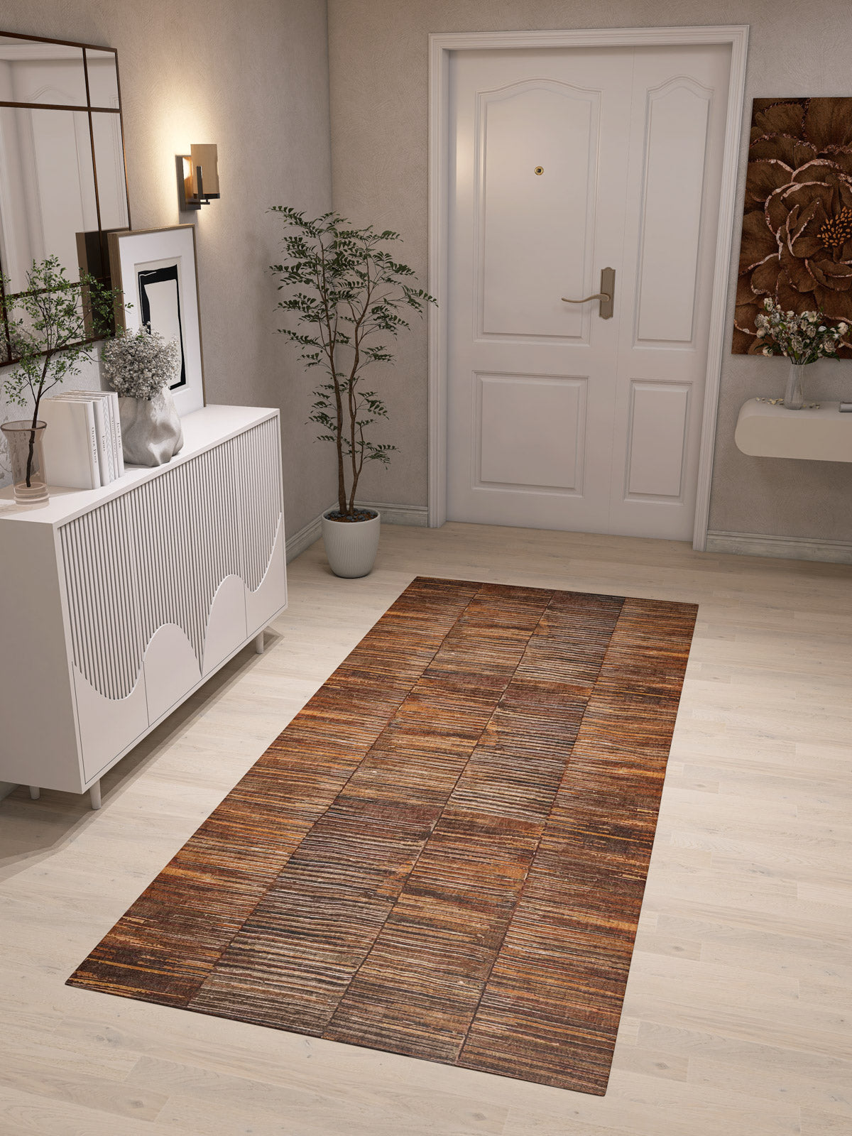 A modern entryway features a white door, the Nostalgic Weft - Washable Rug - JRN33 (Custom Size) in a brown pattern on a light wood floor, a white sideboard with decor, potted plant, wall art, and wall-mounted light—ideal for contemporary spaces.