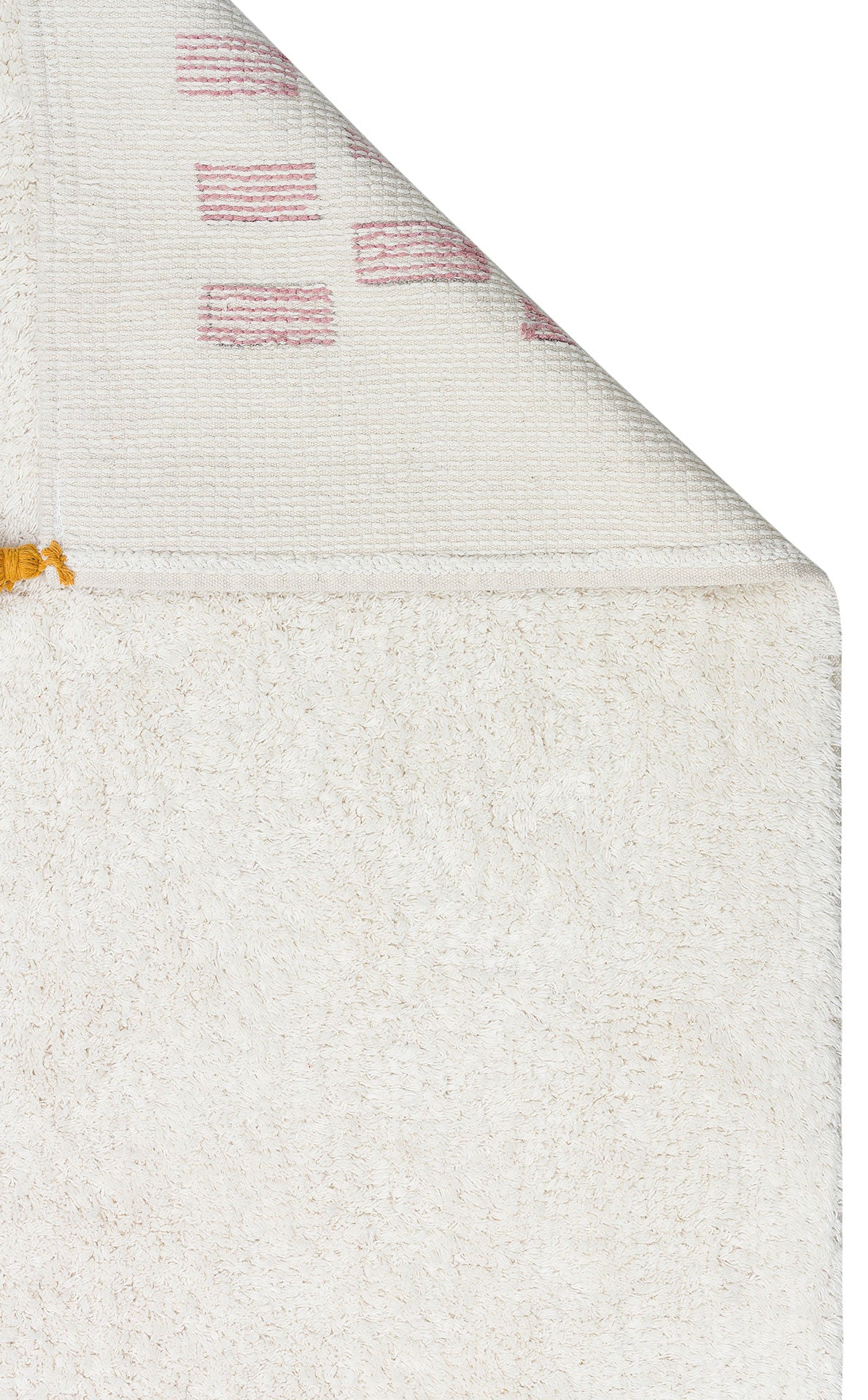 A close-up of the Nursery Nest - Washable Shaggy - CBN04 shows its textured white surface, plush cotton rug feel, a folded top corner with a patterned underside, and a small yellow thread detail near the fold.