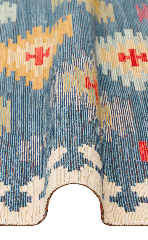 Load image 1 in gallery view. A close-up of the Ocean Form - Washable Reversible Kilim (NMD04) in blue with cream, red, and yellow geometric patterns. The rug curves upward in the middle, showcasing its textured weave and vibrant design.