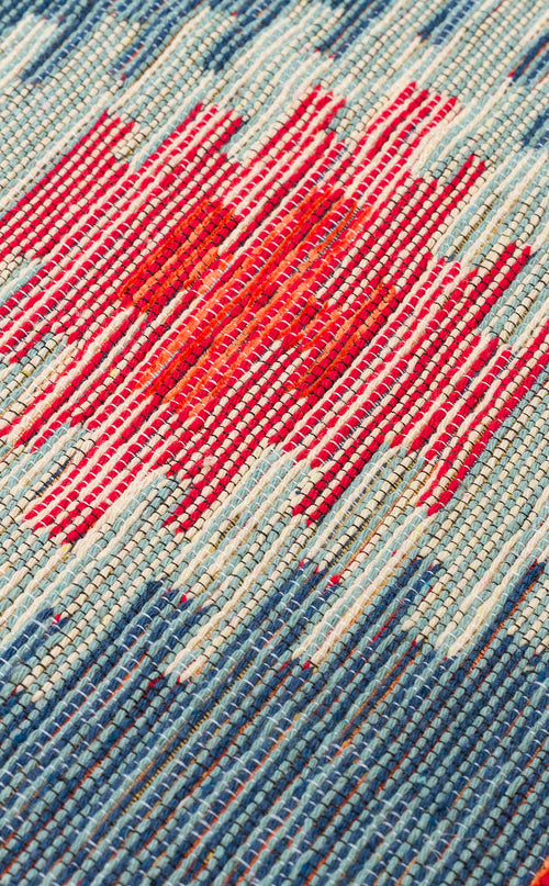 Load image 1 in gallery view. Close-up of the Ocean Form - Washable Reversible Kilim (NMD04) showcasing a woven blue and turquoise tribal pattern with a central red area accented by irregular white stripes.