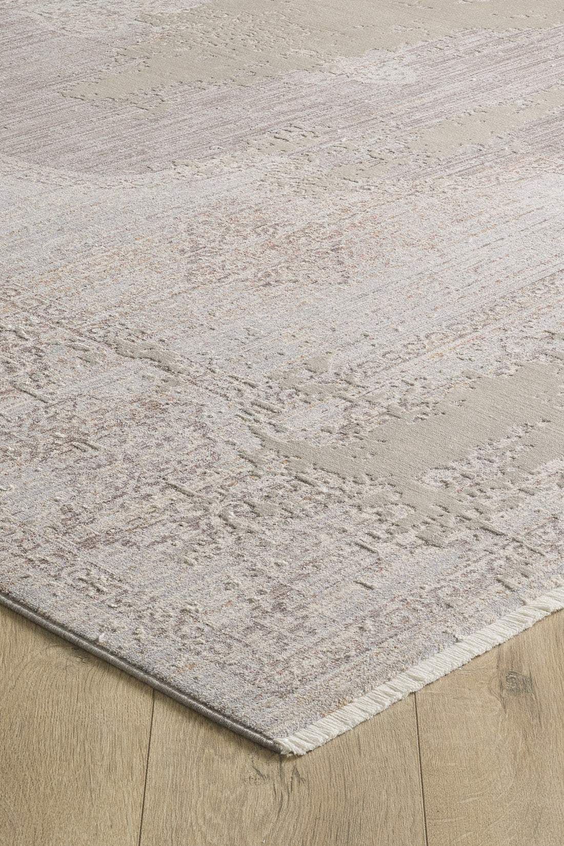 A close-up of the Old World Elegance Modern Rug - Grey - M677N shows its neutral beige, cream, and light brown tones, an abstract distressed pattern, and one-sided fringed edges on a wooden floor. Machine-made design enhances its modern appeal.