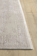 A close-up shows the corner of the Old World Elegance Modern Rug - Grey - M677N, a machine-made viscose polyester rug with subtle patterns and short fringed edges, placed on a wood floor with a natural grain finish.
