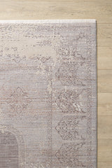 A close-up of the Old World Elegance Modern Rug - Grey - M677N shows its faded vintage-style motifs in beige and gray, with short white fringe along the edge, placed on a light wooden floor.
