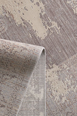 A close-up of the Old World Elegance Modern Rug - Grey - M677N, showcasing its beige, taupe, and gray abstract distressed patterns. One corner is folded to show the underside of this machine-made rug.