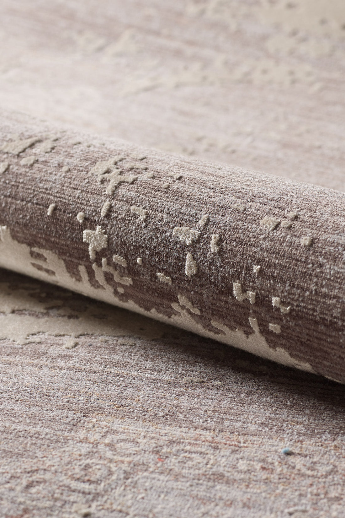 A close-up of the Old World Elegance Modern Rug - Grey - M677N reveals its soft, woven surface, machine-made quality, and subtly raised abstract texture in elegant grey tones. The rug is partially rolled to highlight its distinctive design.