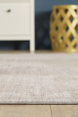 A close-up of the Old World Elegance Modern Rug - Grey - M677N on a wooden floor, with part of a white cabinet on the left and a decorative yellow lattice-patterned stool on the right in soft lighting.