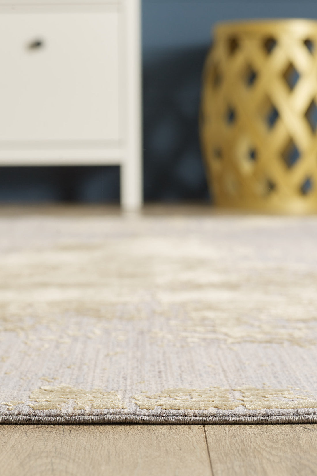 A close-up of the Old World Elegance Modern Rug - Yellow - M677O on a wooden floor, with part of a white cabinet and a decorative yellow stool blurred in the background.