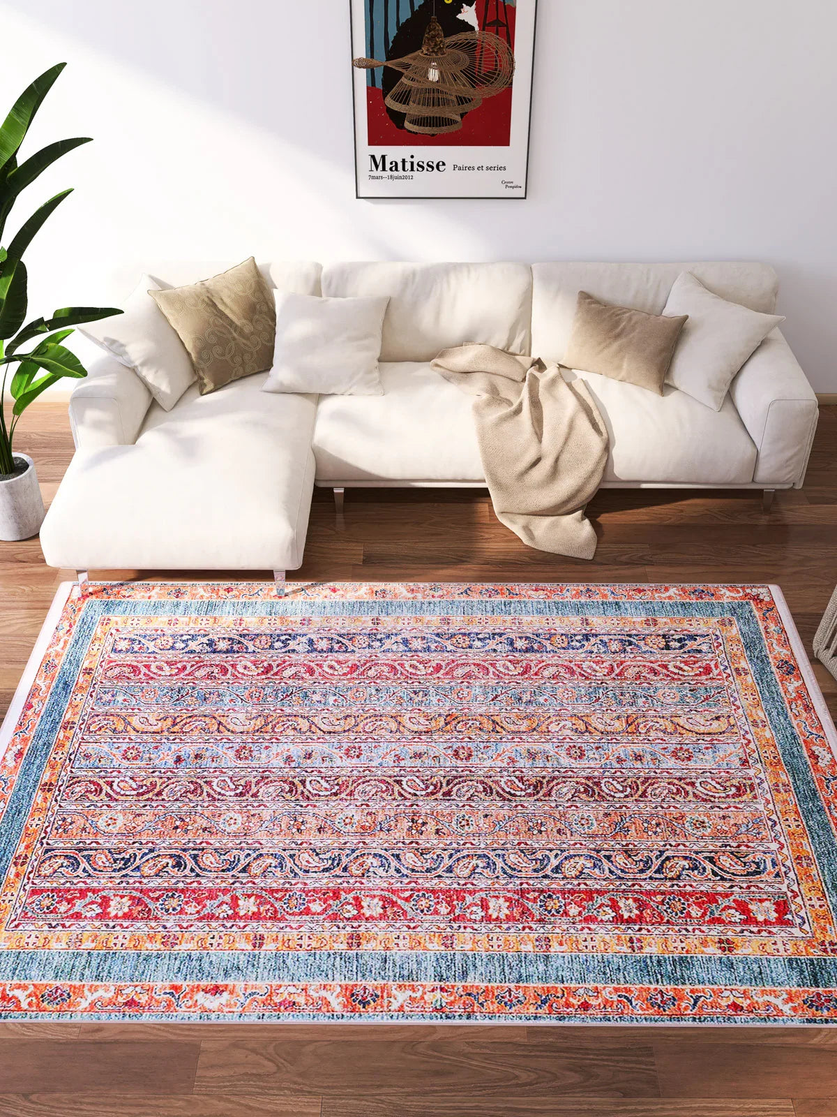 The Old-World Elegance - Washable Rug - JR38 (Outlet) US, featuring a vibrant multicolor pattern, adds charm to your living room with a white sectional, beige cushions, tan throw, green plant, and Matisse art—ideal for high-traffic areas.