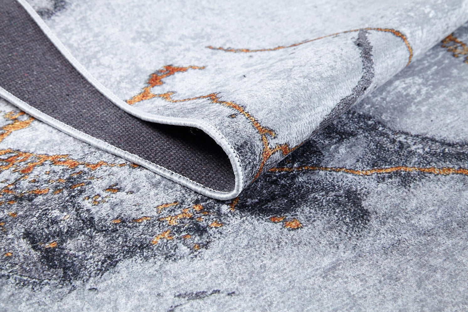 A close-up of the Opulent Veins - Machine-Washable Rug JR1593 (Custom Size) shows its marbled gray texture with orange accents, a folded corner revealing the dark underside, and detailed stitched edging.