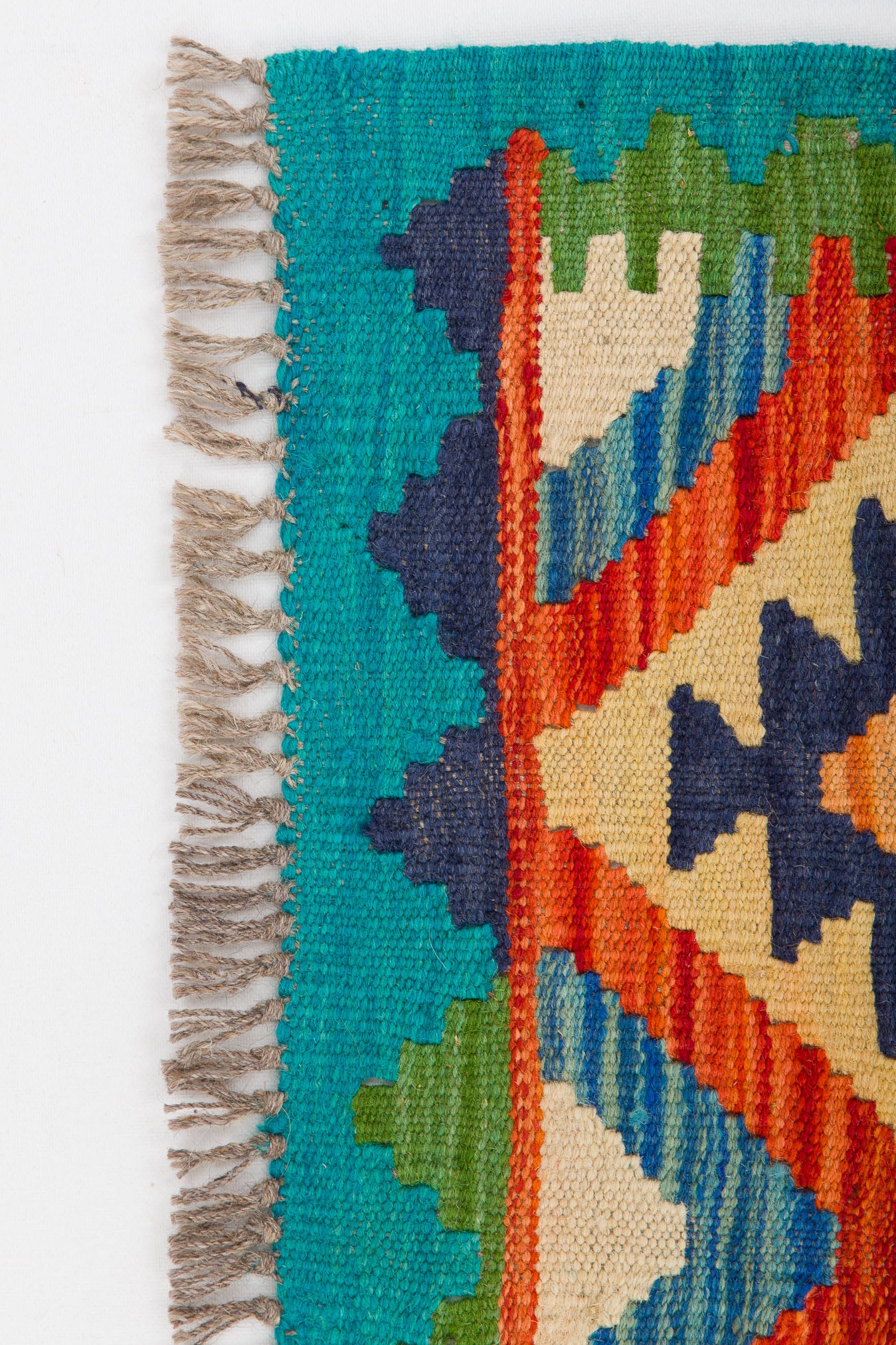 A close-up of the Oriental Harmony - Handwoven Kilim, a colorful flatweave rug featuring geometric patterns in teal, orange, green, cream, navy, and brown fringe on one edge against a white background.