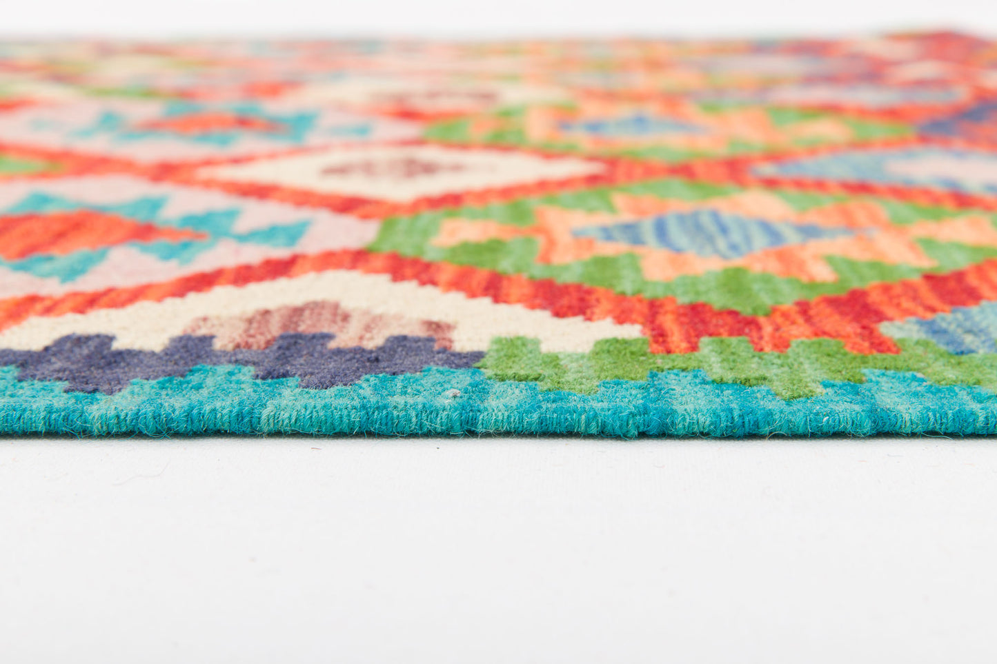 Close-up of the edge of Oriental Harmony - Handwoven Kilim, featuring colorful geometric patterns in blue, green, red, orange, and cream on a white surface.