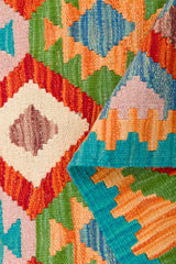 A close-up of the Oriental Harmony - Handwoven Kilim, showcasing its vibrant geometric patterns in red, orange, green, blue, and cream. A folded corner reveals the reverse side of this stunning wool flatweave rug.