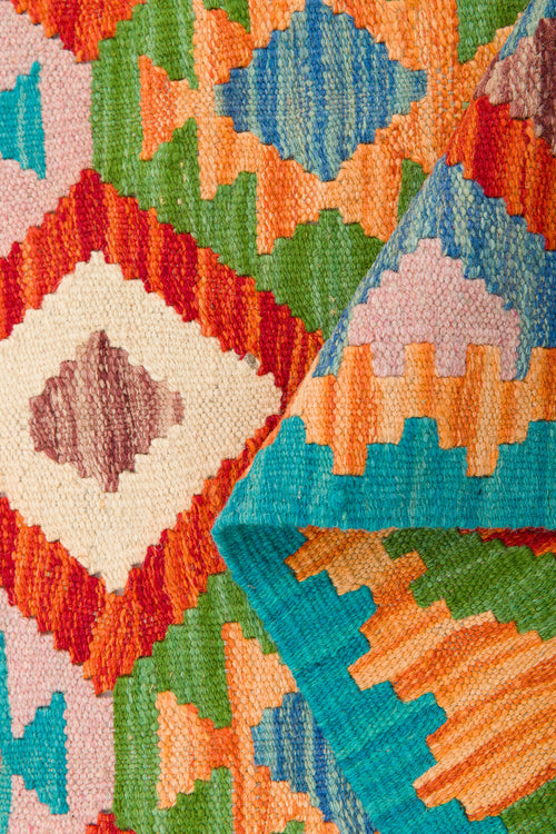 Load image 1 in gallery view. A close-up of the Oriental Harmony - Handwoven Kilim, showcasing its vibrant geometric patterns in red, orange, green, blue, and cream. A folded corner reveals the reverse side of this stunning wool flatweave rug.