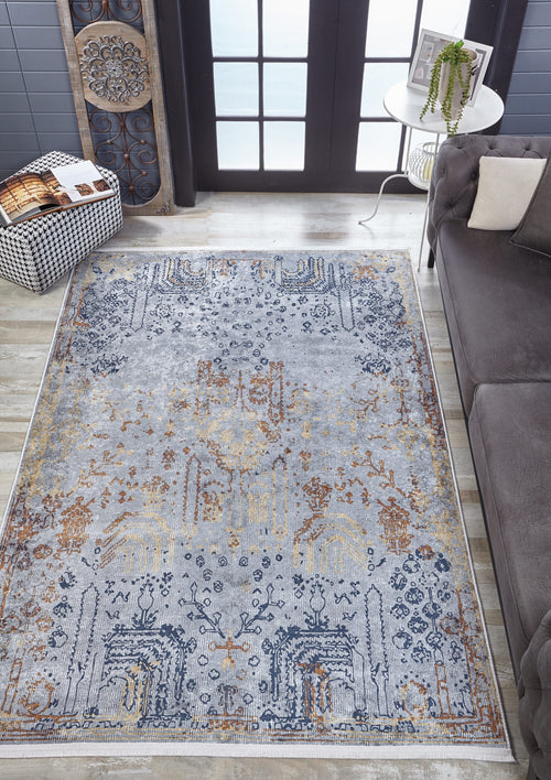 Load image 1 in gallery view. An Oriental Treasures - Machine-Washable Rug JR1613 (Custom Size) with blue, gold, and beige patterns is placed on a light wood floor by a gray sofa, checkered ottoman, and round table with a plant near glass doors.