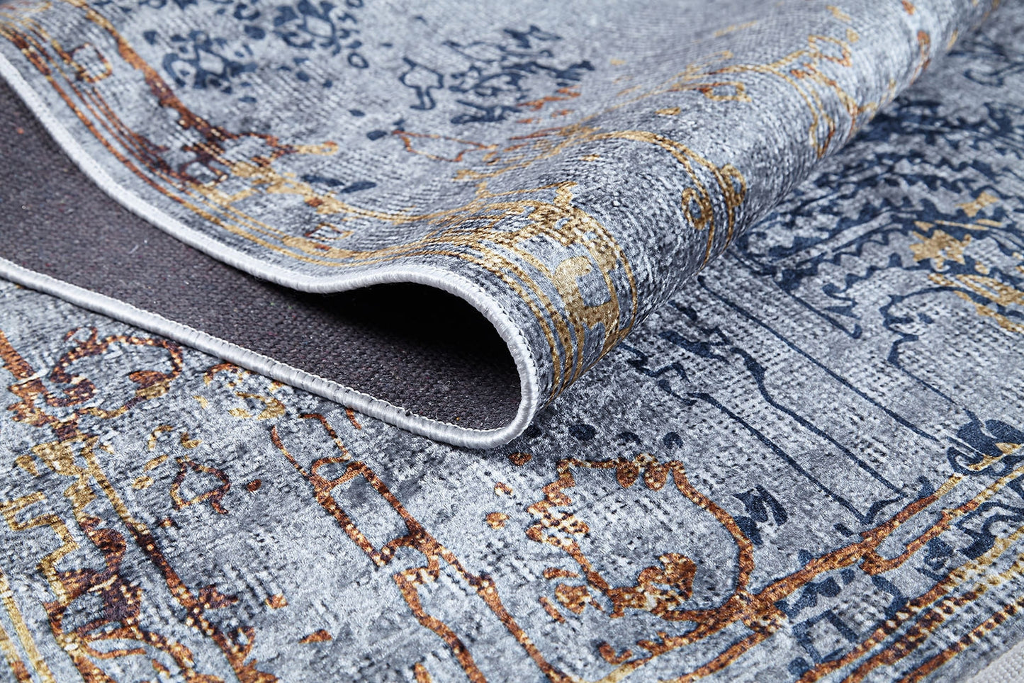 A close-up of the Oriental Treasures - Machine-Washable Rug JR1613 (Custom Size) in gray and gold, partially folded to display its textured abstract design and dark backing. Elegant motifs highlight the rug’s durable, washable surface.