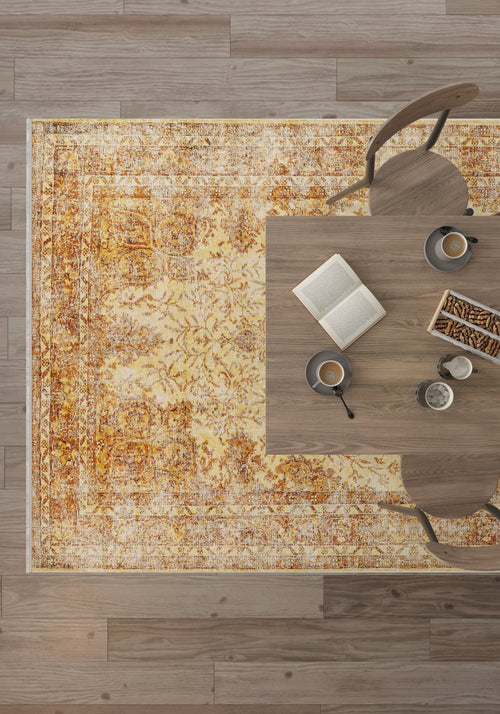 Load image 1 in gallery view. A top-down view shows a wooden table with two chairs, coffee cups, an open book, and snacks on the Ornate Beauty - Washable Rug - JR206 in yellow-gold—perfect for high-traffic areas—set over a wooden floor.