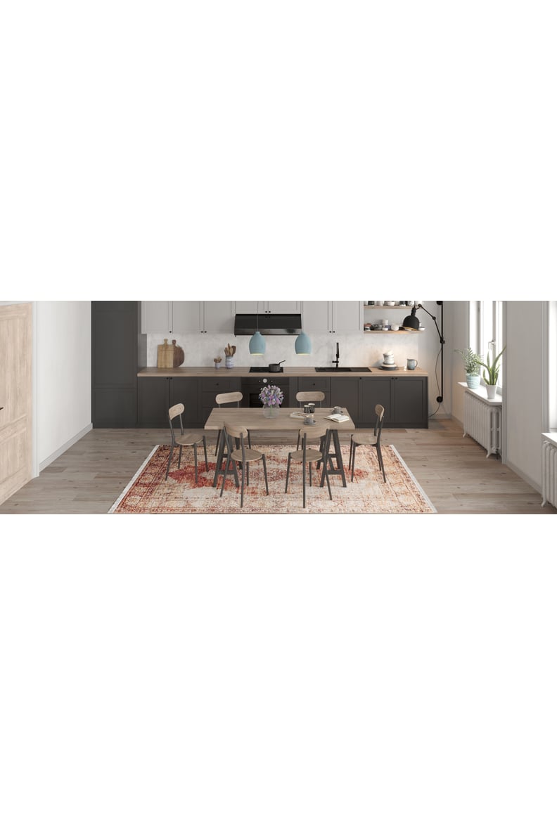 A modern kitchen on light wood floors features the Ornate Grace - Washable Rug - JR1009 (Outlet) US, dark lower cabinets, white uppers, a spacious countertop, pendant lights, a wood dining table, and a vase of purple flowers adding vibrancy—ideal for busy spaces.