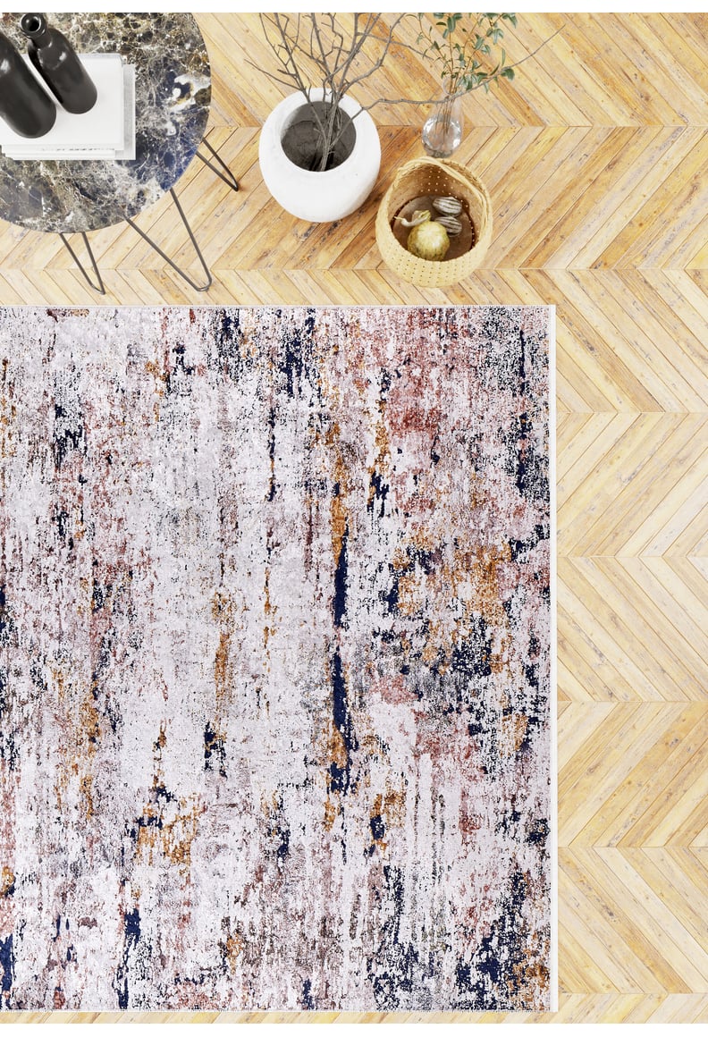 The Painted Dreams - Washable Rug - JR432 (Custom Size), featuring white, beige, rust, and navy patterns, sits on a light wood herringbone floor and is styled with a round marble table, white vase with branches, and a woven basket of lemon and lime.