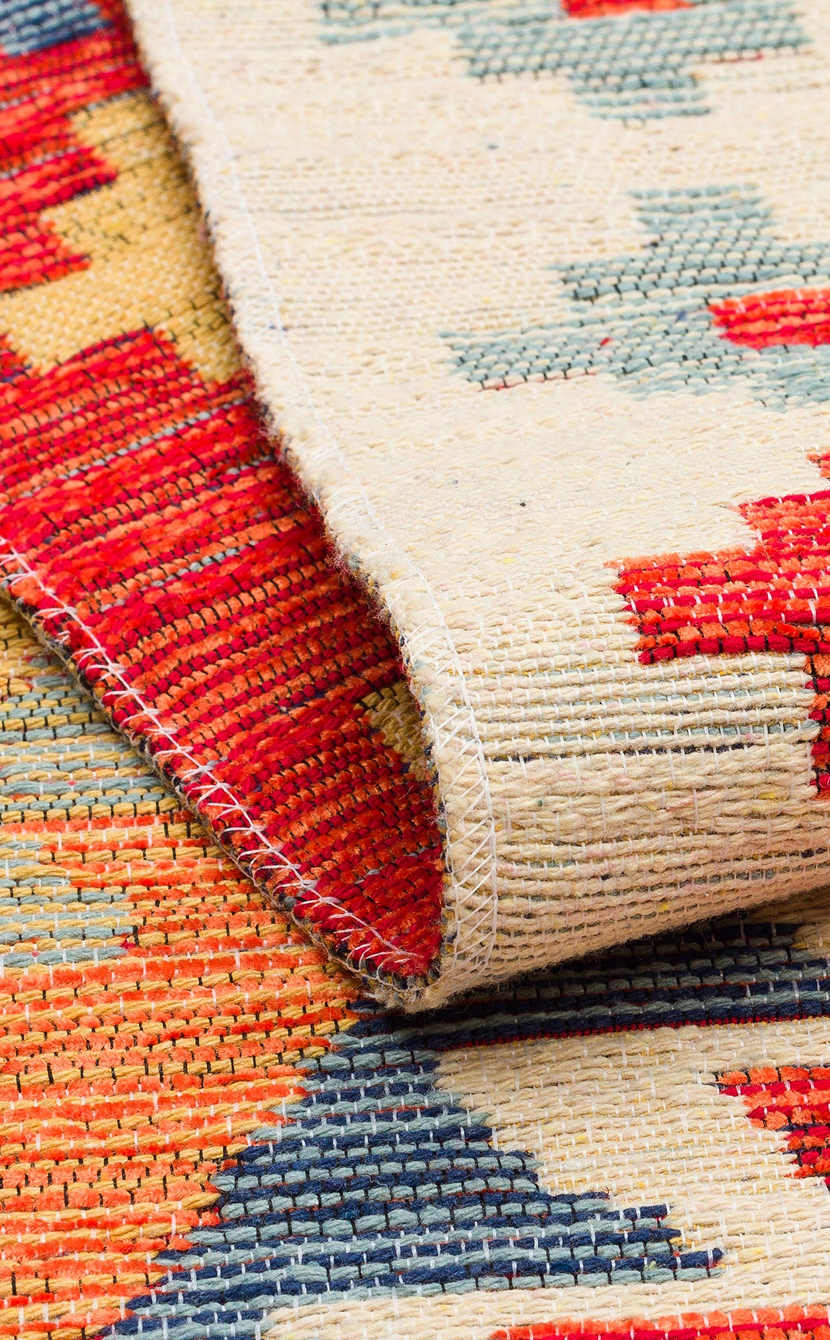 A close-up of the Pastel Grid - Washable Reversible Kilim (NMD09) rug shows its geometric patterns in red, beige, blue, and orange. A folded corner highlights the textured weave and stitching details of this washable kilim.