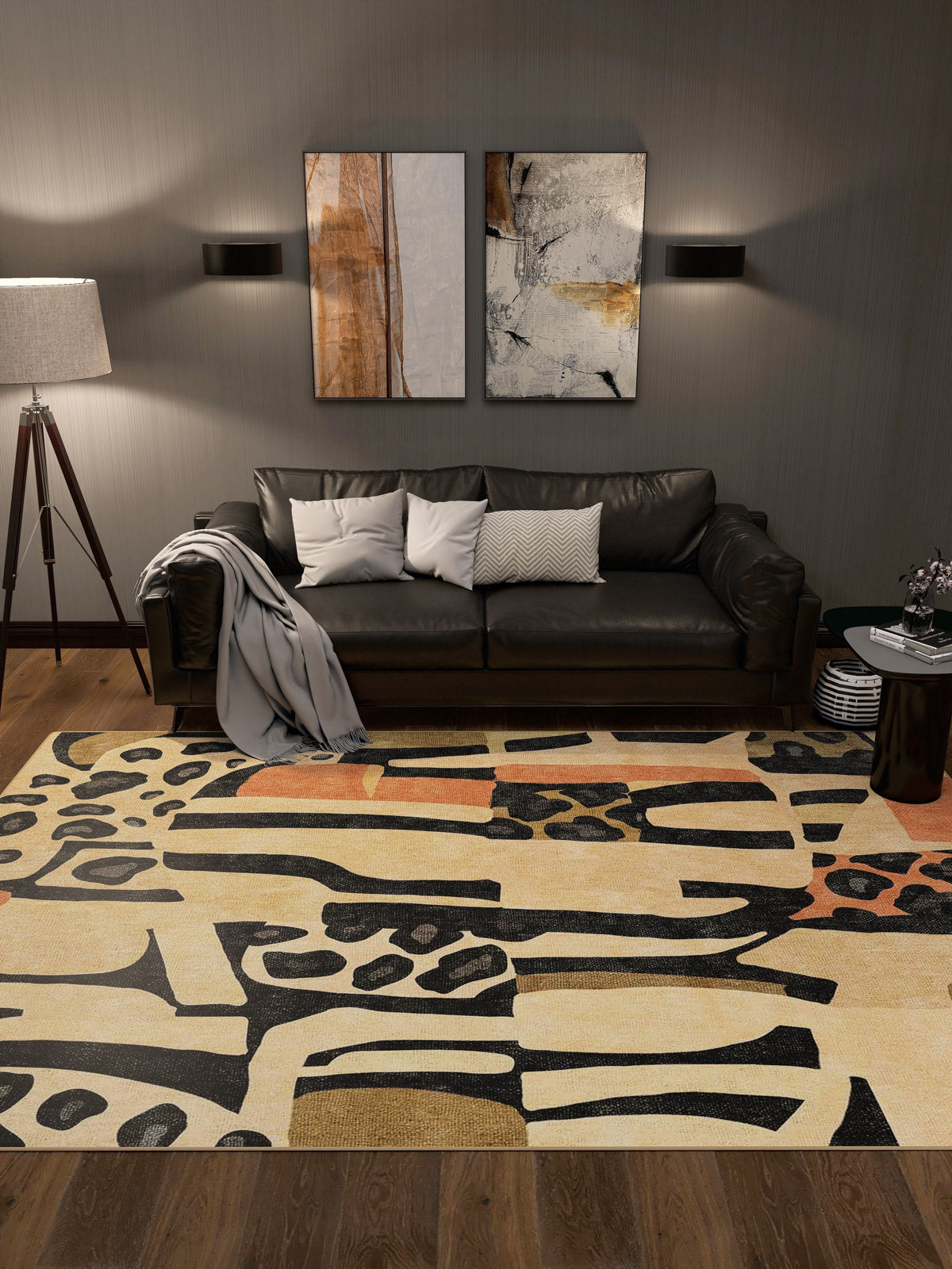 A modern living room with a black sofa, neutral cushions, a grey throw, two abstract wall artworks, a floor lamp, a small round side table with books, and the Pastel Harmony - Washable Rug - JRN43 featuring black and beige patterns.