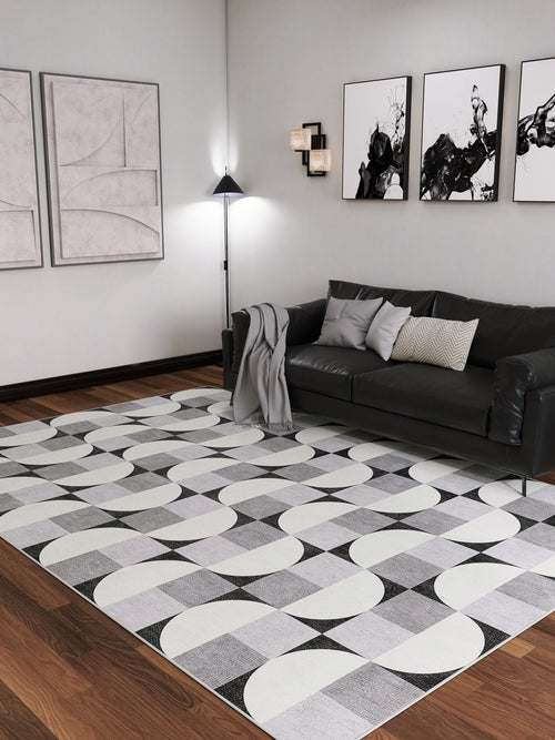 Load image 1 in gallery view. A modern living room with a black sofa, gray throw blanket, abstract wall art, floor lamp, wooden flooring, and the Patina Bloom - Washable Rug - JRN50. The space has a minimalist monochrome design with clean lines and contemporary decor.