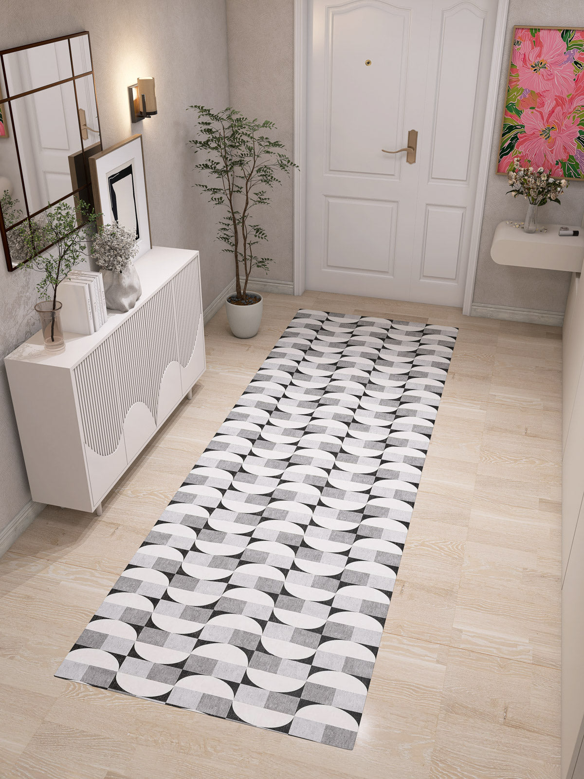 A modern hallway features light wood floors, the Patina Bloom Washable Rug - JRN50 (Custom Size), a potted plant, sleek white sideboard with decor, wall art, and a white front door with gold handle for chic interiors.