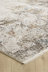 A close-up of the Pebble Pathway Premium Area Rug - M683L showcases its modern abstract, mottled pattern in neutral beige, gray, and brown tones on a light wood floor, with a visible machine-made edge and short fringe.