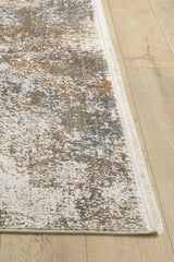 A close-up of the Pebble Pathway Premium Area Rug - M683L, a machine-made abstract rug with a speckled neutral pattern accented by blue and rust, features a thin white fringe along one edge and lies on a light wood floor.