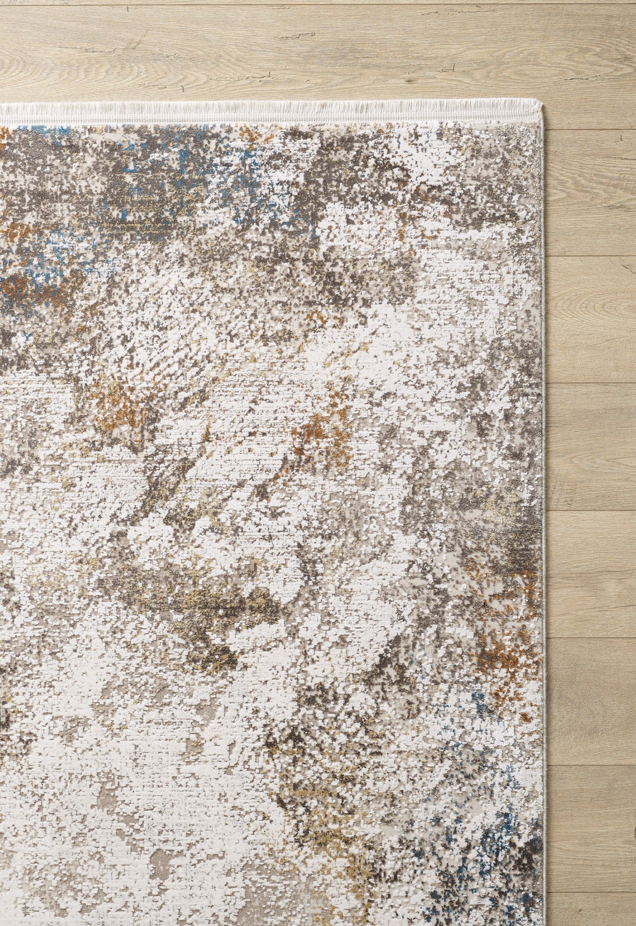 A close-up of the Pebble Pathway Premium Area Rug - M683L, featuring a machine-made abstract speckled pattern in white, beige, brown, and gray, showcased on a light wood floor.