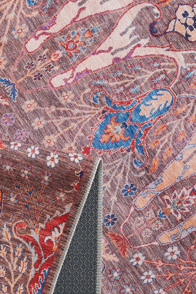 A close-up of the Peregrine Peachy Brown Washable Rug - LCC3022 (Outlet) US shows intricate floral and animal patterns in pink, blue, and cream, with a folded corner revealing its textured, dark grey underside.