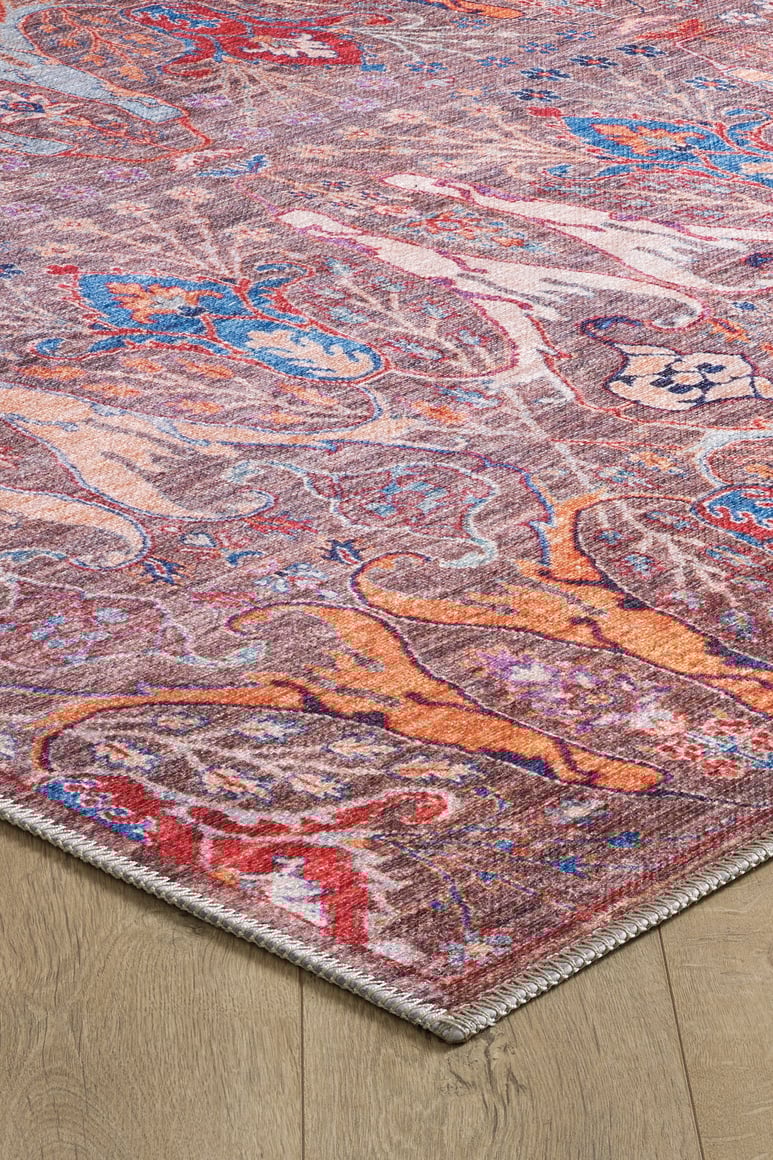 A close-up of the Peregrine Peachy Brown Washable Rug (LCC3022, Custom Size) shows its vibrant red, blue, orange, and purple accents and woven pattern on a wooden floor—ideal for high-traffic areas.