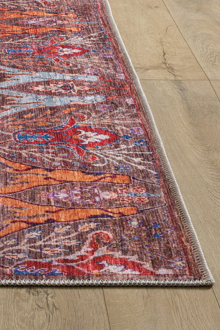 A close-up of the Peregrine Peachy Brown Washable Rug - LCC3022 (Custom Size) shows its colorful orange, red, and blue designs with a stitched border on wood flooring—a vintage-inspired rug perfect for stylish, high-traffic areas.