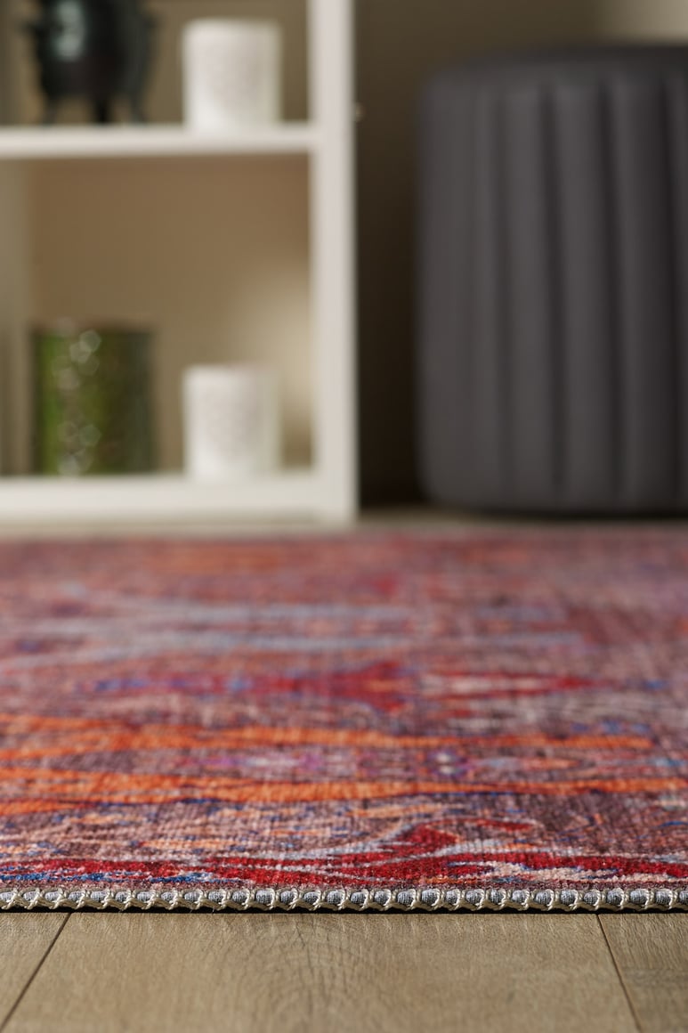 A close-up of the Peregrine Peachy Brown Washable Rug - LCC3022 (Custom Size) on a wooden floor, with a white shelving unit and gray ottoman in the background—perfect for high-traffic spaces.