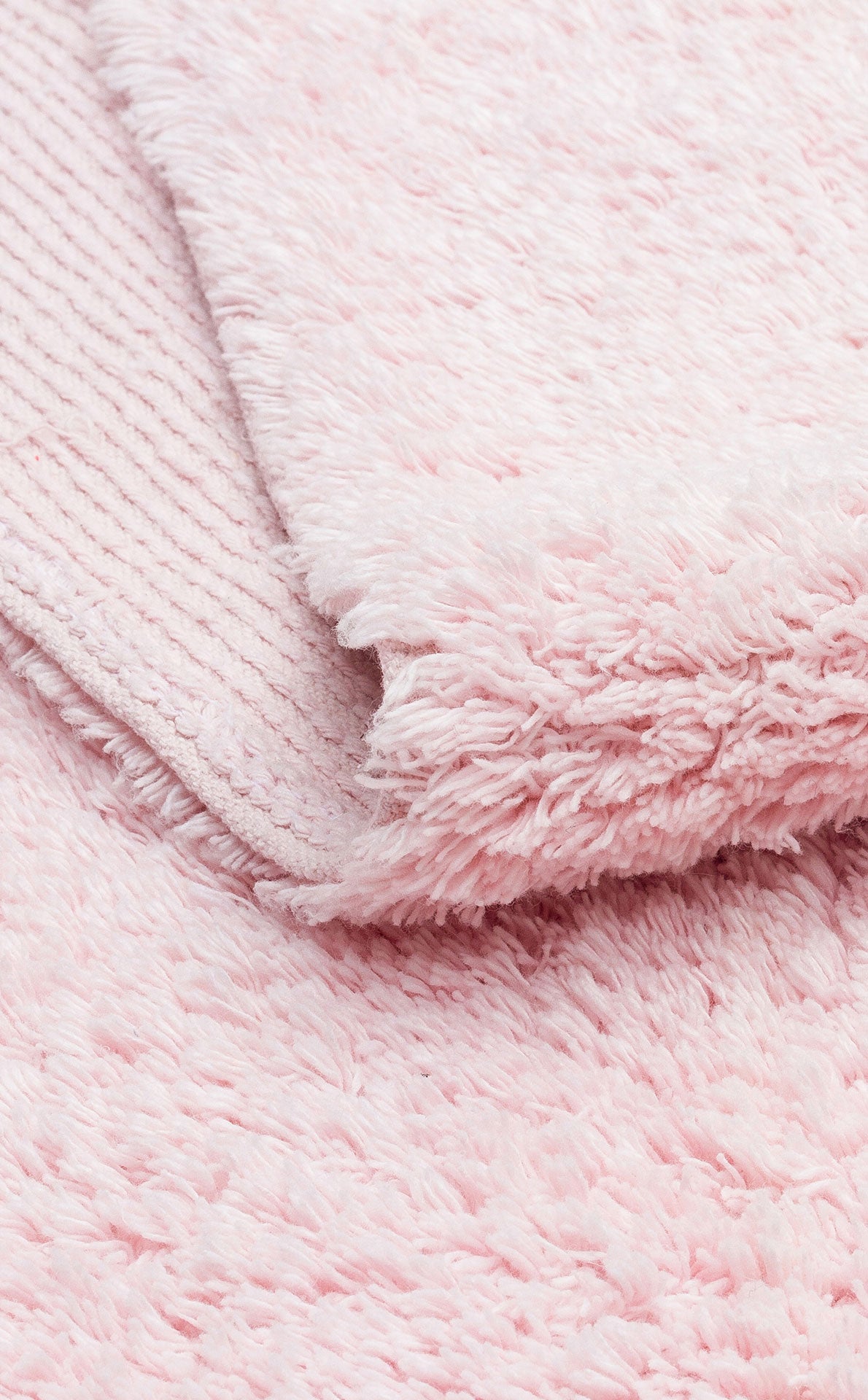 A close-up of Powder Calm - Washable Shaggy - CBNPLAIN shows its soft, fluffy light pink texture, with one edge folded to reveal a ribbed underside contrasting the plush surface.
