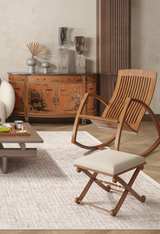 A modern living room with a curved wooden chair, cushioned stool, low coffee table with snacks, an ornate red lacquered Asian-inspired cabinet, and the allergy-sensitive Pure Bliss - Washable Rug - JR745 (Custom Size) in cream and beige.