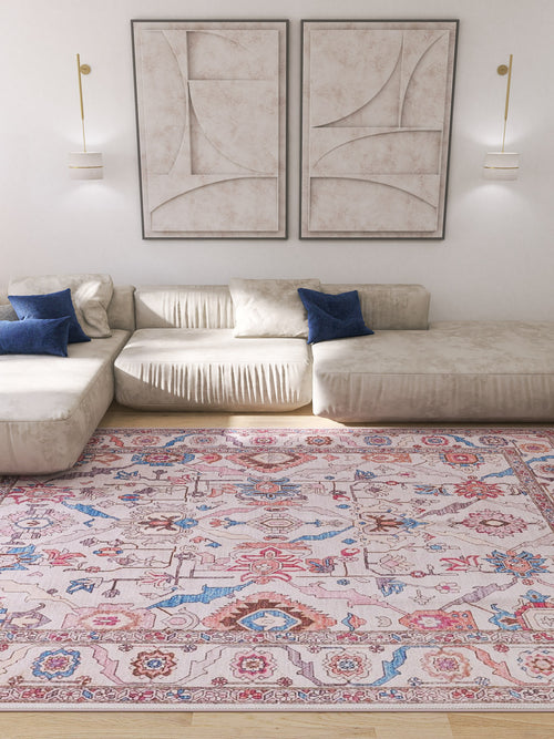 Load image 1 in gallery view. A modern living room with a cream sectional sofa, blue accent pillows, abstract wall art, wall-mounted lights, and the Quasar Traditional Washable Rug - LCC3024 with colorful patterns on a wooden floor.