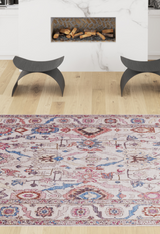 A living room scene featuring the Quasar Traditional Washable Rug - LCC3024 in red, blue, and beige on a light wood floor, flanked by two modern black stools and a white fireplace with stacked wood inside.