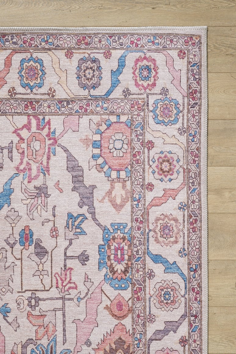 A close-up of the Quasar Traditional Washable Rug - LCC3024 shows its pink, blue, and beige geometric and floral patterns on a light wooden floor. This washable rug combines charm with practicality for any space.