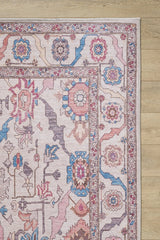 A close-up of the Quasar Traditional Washable Rug - LCC3024 shows its pink, blue, and beige geometric and floral patterns on a light wooden floor. This washable rug combines charm with practicality for any space.