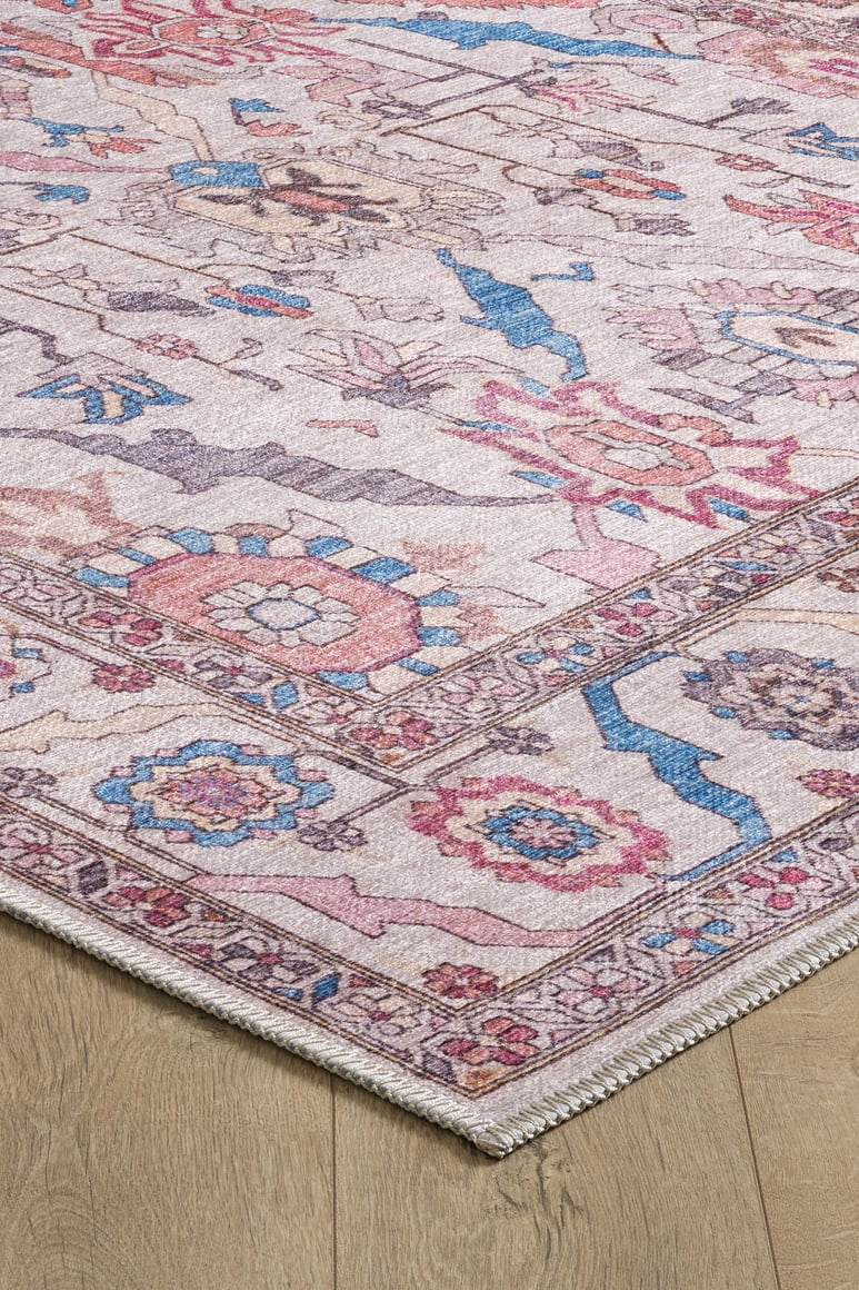 A close-up of the Quasar Traditional Washable Rug - LCC3024, a pastel flat weave with pink, blue, and beige floral and geometric patterns, shown on light wood flooring.
