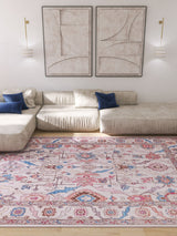 A modern living room with a cream sectional sofa, blue accent pillows, the Quasar Traditional Washable Rug - LCC3024 (Custom Size) for high-traffic areas, abstract wall art, two wall-mounted lamps, and bright natural light.