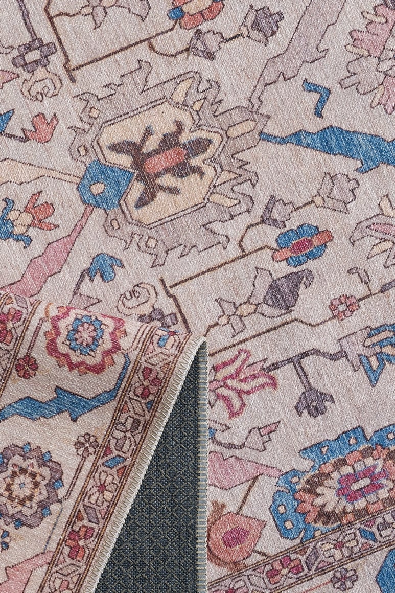 A close-up of the Quasar Traditional Washable Rug - LCC3024 (Custom Size) shows its pastel patterns and detailed border, with one corner flipped to reveal a blue non-slip backing—ideal for high-traffic areas.
