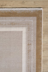 A close-up of the Radiant Edges Bordered Rug - Amber (M542G), showcasing its beige, ivory, and light brown geometric borders on a light wood floor. The rug has a textured, slightly distressed finish with a classic border design.